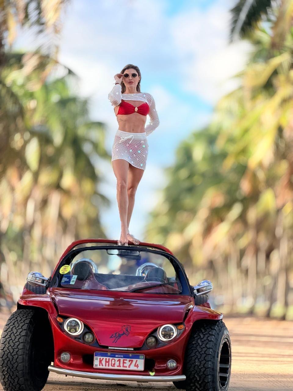 Cliente posando sobre o buggy vermelho do Porto Buggy Naldo no coqueiral de Porto de Galinhas
