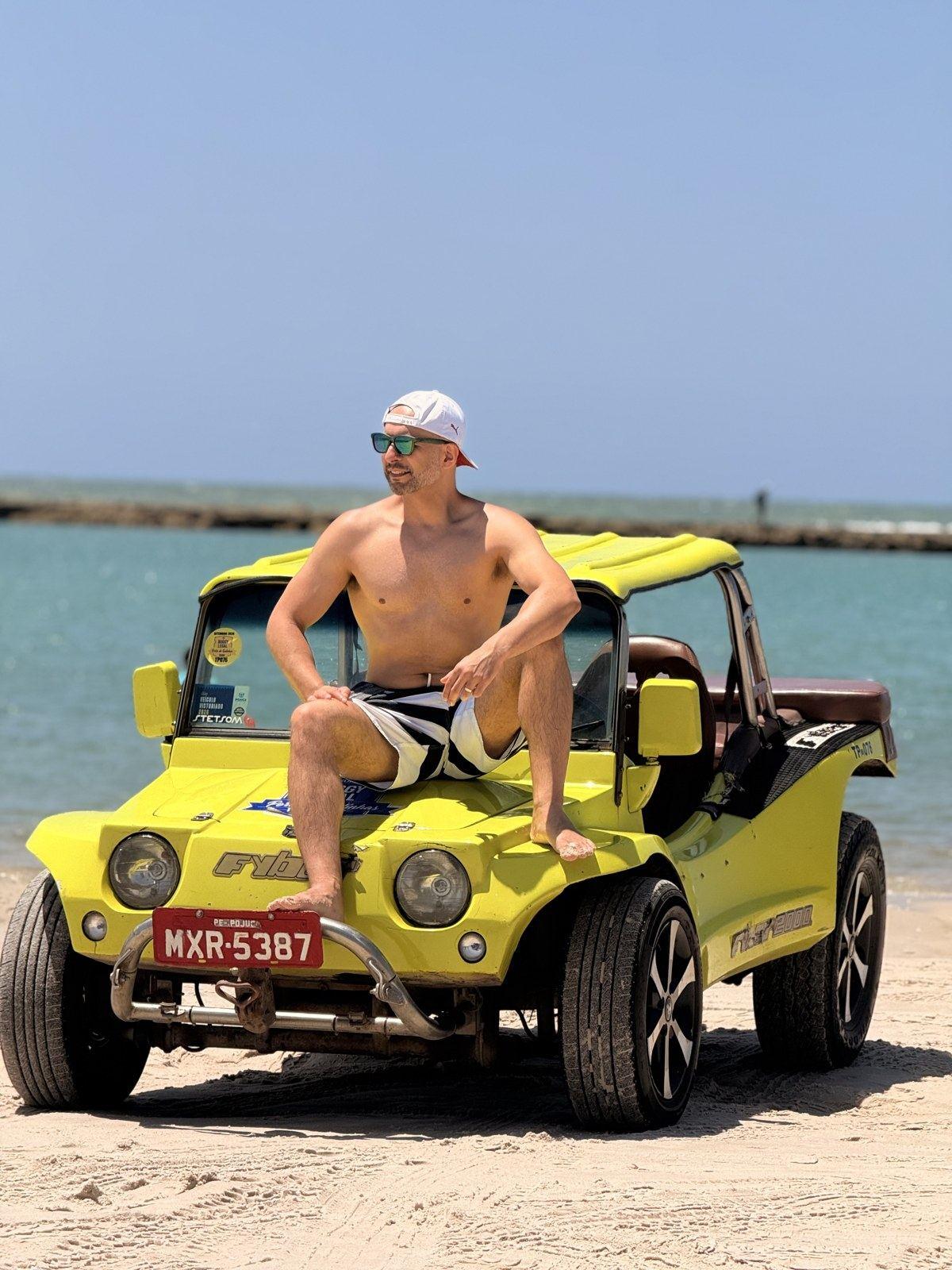 Cliente sentado no capô do buggy amarelo em frente ao mar
